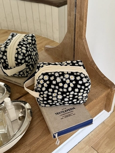 Black canvas cosmetic bag with white daisy prints and cream zipper on a book