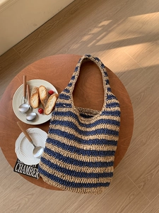 Flat lay of a woven striped tote bag on a wooden table with bread and coffee