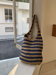 Detailed texture of blue and beige woven straw shoulder bag against a bright window