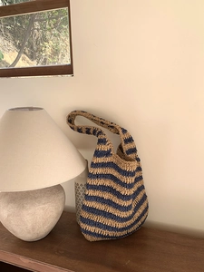 Detail of blue and beige woven bucket bag with sturdy handles on a wooden table