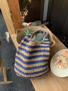 Detail of a large straw woven beach tote featuring blue and beige striped patterns