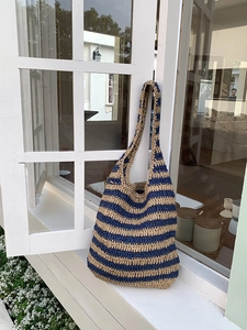 Close-up of contrast-color woven shoulder bag with navy and khaki stripes on white window