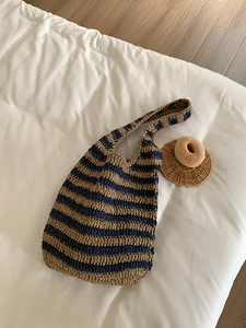 Detail of woven straw shoulder bag with navy blue and wood stripes on white bedding