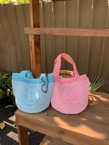 Close-up of handmade crochet mini bags featuring yellow smiley faces on a wooden bench