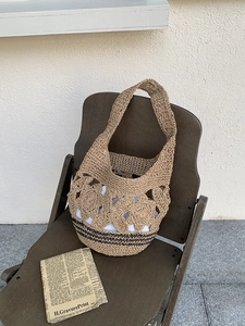 Détail de fleurs ajourées au crochet et rayures noires sur un sac fourre-tout en paille