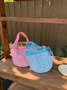 Detail of handmade knit tote bags in pink and blue featuring iconic smiley face patterns