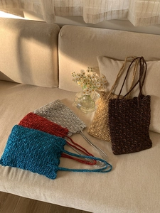 Detail of colorful metallic woven tote bags in blue, red and gold on a cozy white sofa