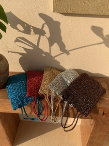 Close-up of handmade woven bags in five metallic colors on a rustic wooden bench