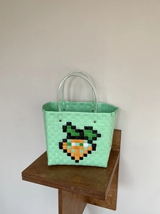 Detail of mint green hand-woven bag with pixel carrot motif and clear plastic handles