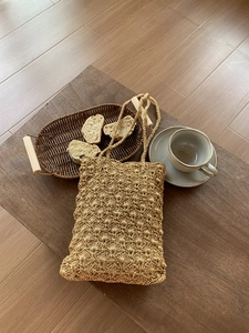 Detailed view of golden hand-woven shoulder bag with intricate shell pattern on a wooden table