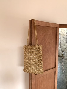 Macro detail of hand-woven gold shoulder bag showing intricate crochet fan pattern texture