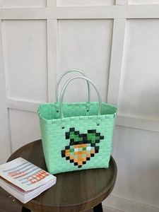 Detail of hand-woven green tote bag featuring carrot pixel art and transparent handles