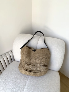 Detail of hand-woven straw tote with hollow pattern and black leather strap on sofa