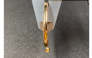 Detail view of caliper measuring the thickness of a gold circular pendant necklace