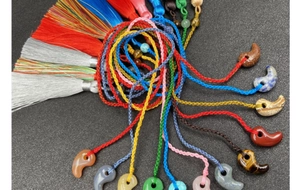 Makro-Detail verschiedener Magatama-Steinanhänger mit bunten Seidenquasten auf dunklem Grund