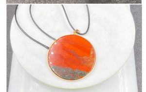 Macro shot of circular red jasper stone pendant with gold bezel on black cord