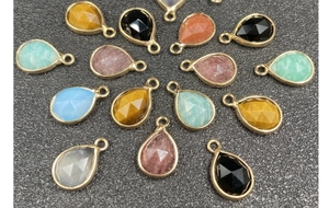 Flat lay of colorful teardrop gemstone pendants with gold plated edges for jewelry making