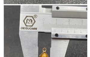 Macro view of teardrop gemstone pendant width measurement using silver calipers