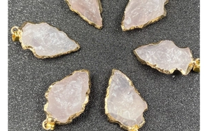 Détail des pendentifs pointe de flèche en quartz rose avec bords dorés sur fond sombre