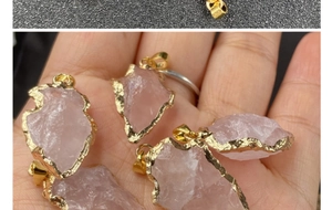 Gros plan de pendentifs flèches en quartz rose brut avec bords dorés dans la main