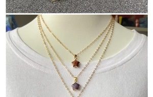 Layered gold chain necklace featuring purple and brown star stone pendants on a white shirt