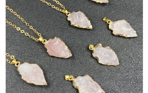 Gros plan de pendentifs en quartz rose en forme de flèche avec bordures dorées sur fond noir
