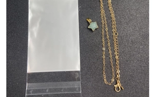 Detail of gold star pendant necklace with green crystal and clear plastic packaging
