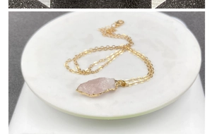 Gros plan d'un pendentif en cristal rose brut avec bords dorés dans un bol blanc
