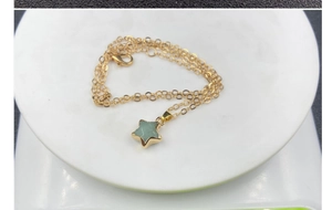 Detailed view of a green crystal star pendant with gold trim on a delicate chain necklace