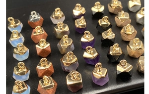 Macro shot of assorted hexagonal gemstone pendants with gold plated metal caps on black texture