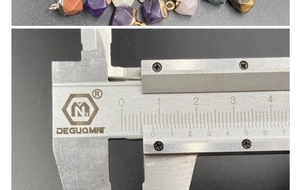 Detailed measurement of multi-color crystal pendant size with calipers on gray background
