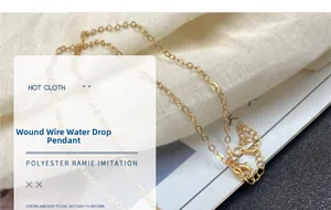 Primer plano del collar con colgante de gota de agua envuelto en alambre dorado en tela