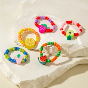 Detailed close-up of five colorful fruit-themed beaded rings on white stone textures
