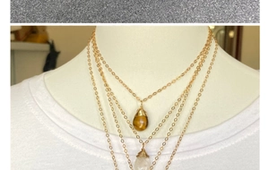 Primer plano de collar dorado de tres capas con colgantes de gota de ojo de tigre y cuarzo