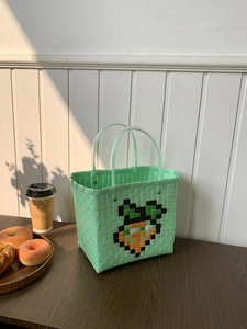 Detail of mint green hand-woven tote bag with pixel carrot pattern on wooden surface