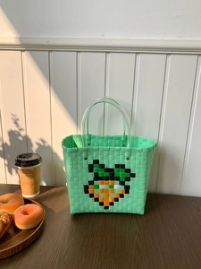 Detail of mint green woven beach bag featuring a pixel carrot design and clear handles