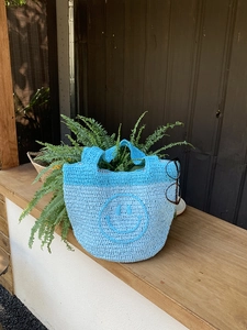 Detail of blue crochet tote bag with a woven smiley face on a rustic wooden table