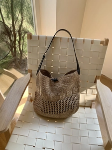 Detail of hand-woven straw beach bag with hollow crochet pattern and black leather strap