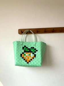 Detail of woven beach tote showing pixel carrot pattern and transparent handle grips