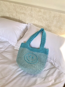 Close-up of handmade crochet tote bag with teal gradient and smile face pattern
