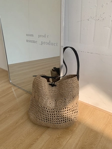 Close-up of handmade woven straw beach bag featuring crochet flower patterns and horn buckle