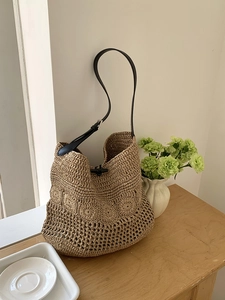 Detail of hollow woven beach bag featuring a black horn button closure and leather strap