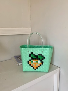 Detail of mint green woven tote bag featuring an orange pixel carrot pattern on the front