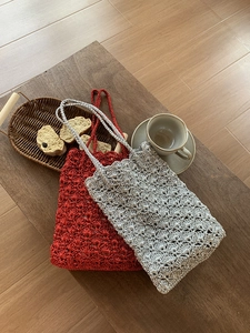 Detail of handmade knit tote bags in red and silver on a wooden table with tea setting