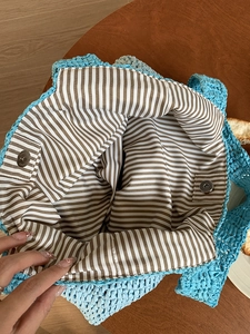 Handmade light blue crochet bag with striped lining and magnetic closure on wood surface