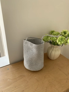 Détail d'un sac seau tissé argenté avec lustre métallique sur une table en bois