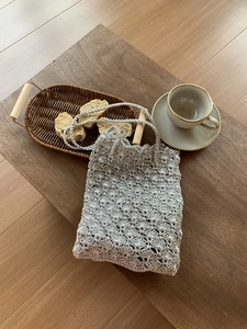 Detailed close-up of a silver woven bag with intricate crochet shell patterns on wood