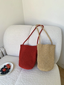 Détail de sacs seaux tissés à la main en rouge foncé et or champagne sur sofa