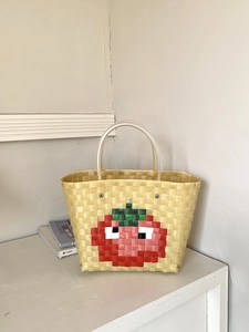 Detail of handwoven beach bag with pixelated tomato design and round transparent handles