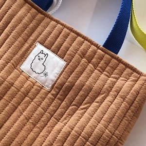 Détail du tissu matelassé marron avec écusson alpaga et poignées en sangle colorées